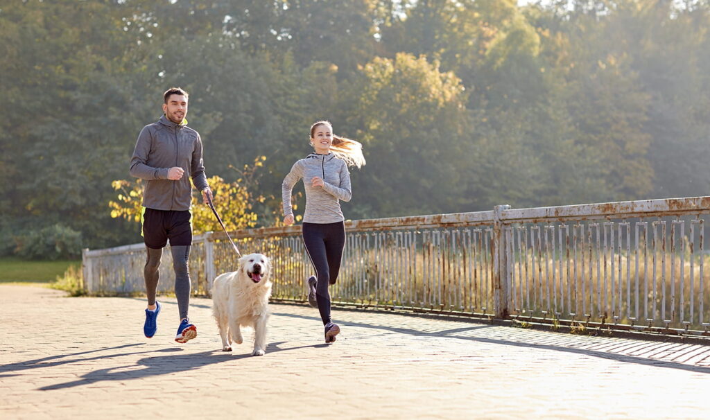 two people jogging with a dog